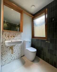 Compact bathroom in Geelong featuring terrazzo flooring, dark tiled walls, and modern fixtures, designed by Bay Plumbing and Drainage.