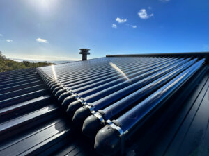 Solar rod and tube hot water system panel on a black roof with the sun reflecting off the glass tubes, with the blue sky in the background 