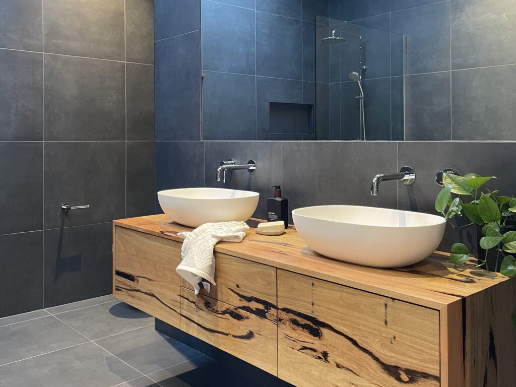 Bay Plumbing and Drainage's Modern Bathroom Renovations and Installations with twin vessel sinks on a wooden vanity unit, set against dark grey tiles in Geelong.