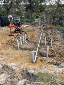 Trenches being dug with concrete piers installed, likely part of a slab or drainage foundation system.