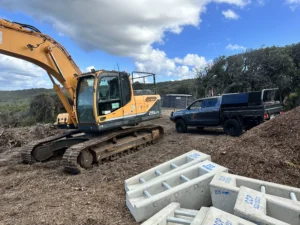 Excavator and truck on a construction site with large white drainage pits placed on the ground.