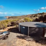 Large corrugated steel water tank installed on a coastal property for rainwater harvesting.