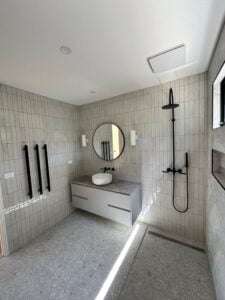 An Elegant Bathroom in Geelong with a wall-mounted basin and black fixtures, expertly installed by Bay Plumbing and Drainage.