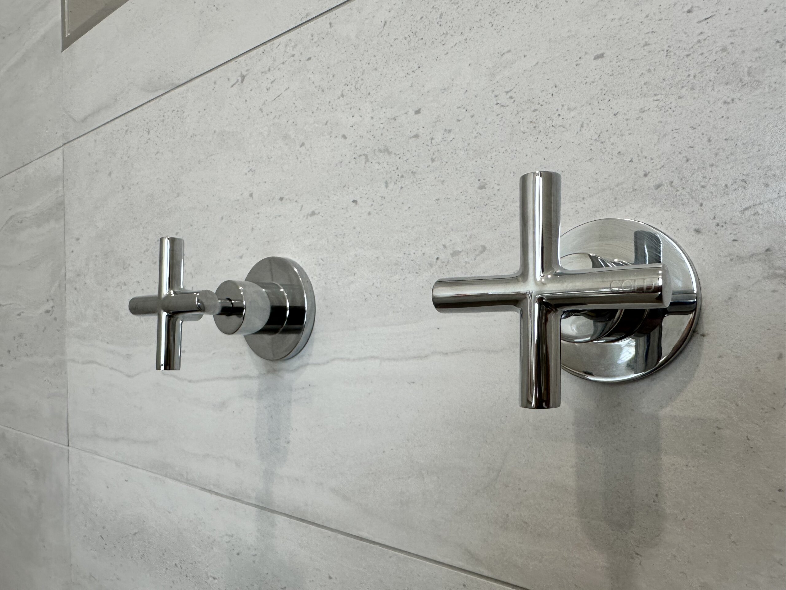Close up photo of T handle shower taps with a grey tile in the background in a shower 