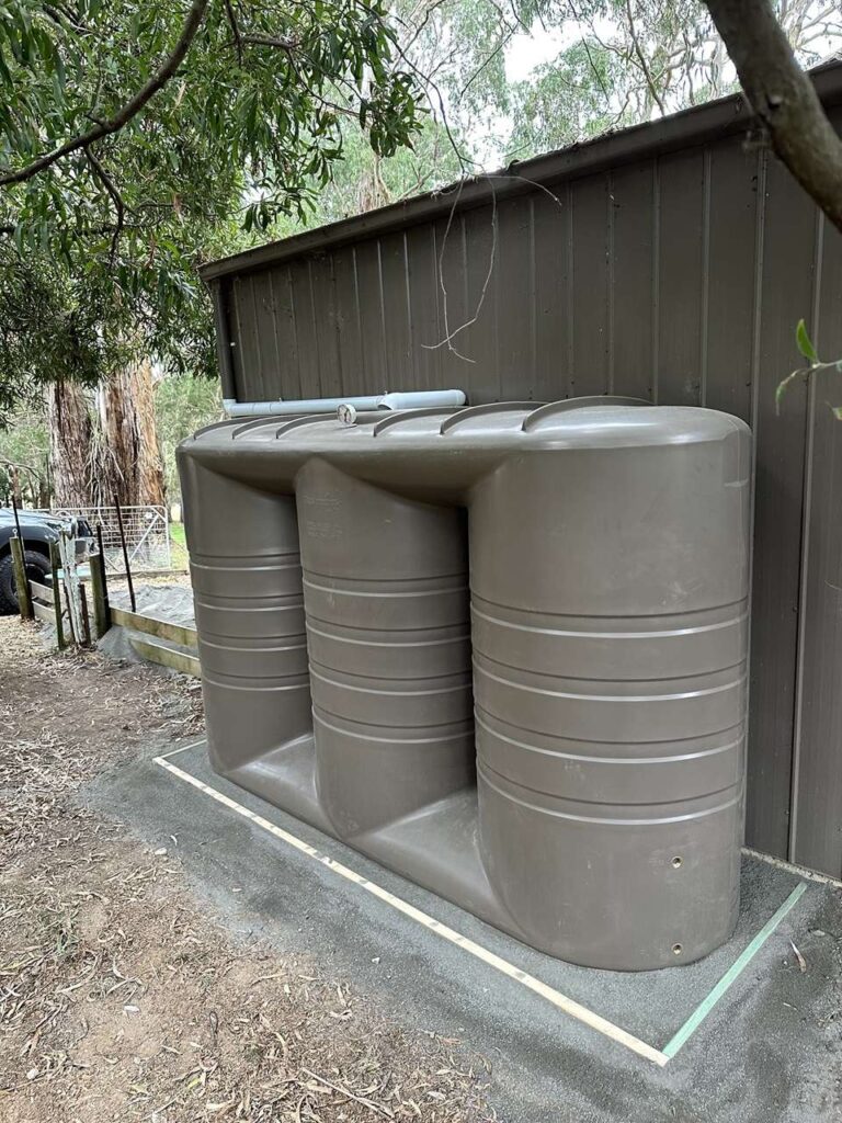 Slimline poly rainwater tanks installed next to a shed for efficient water storage.