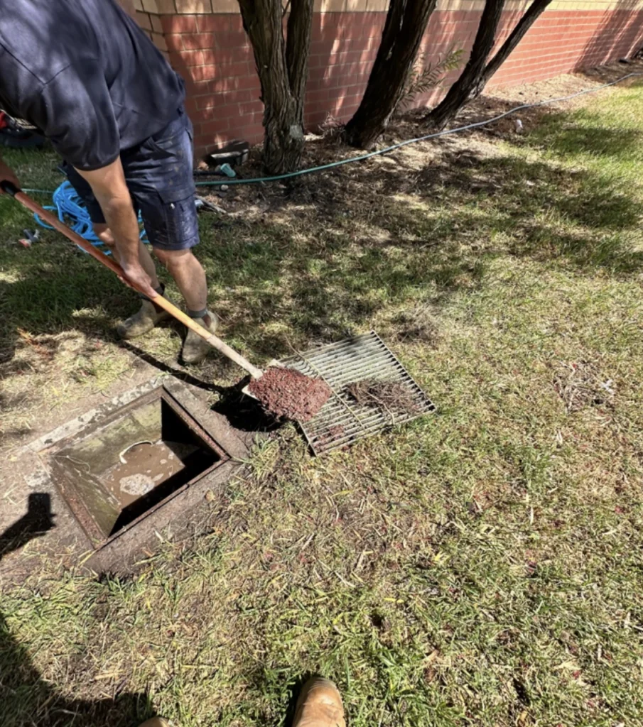 One of Bay Plumbing and Drainage's plumber in action clearing a sewer grate of debris to prevent blockages in Geelong.