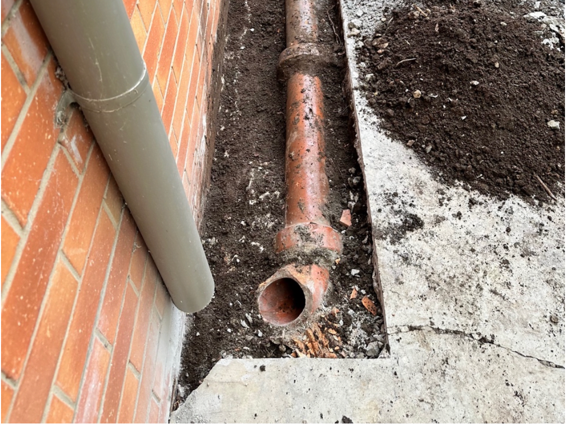 Excavated broken underground pipe next to brick wall, showing emergency pipe replacement.