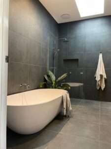 Modern bathroom in Geelong featuring a standalone bathtub, dark grey tiles and shower, designed and installed by Bay Plumbing and Drainage.