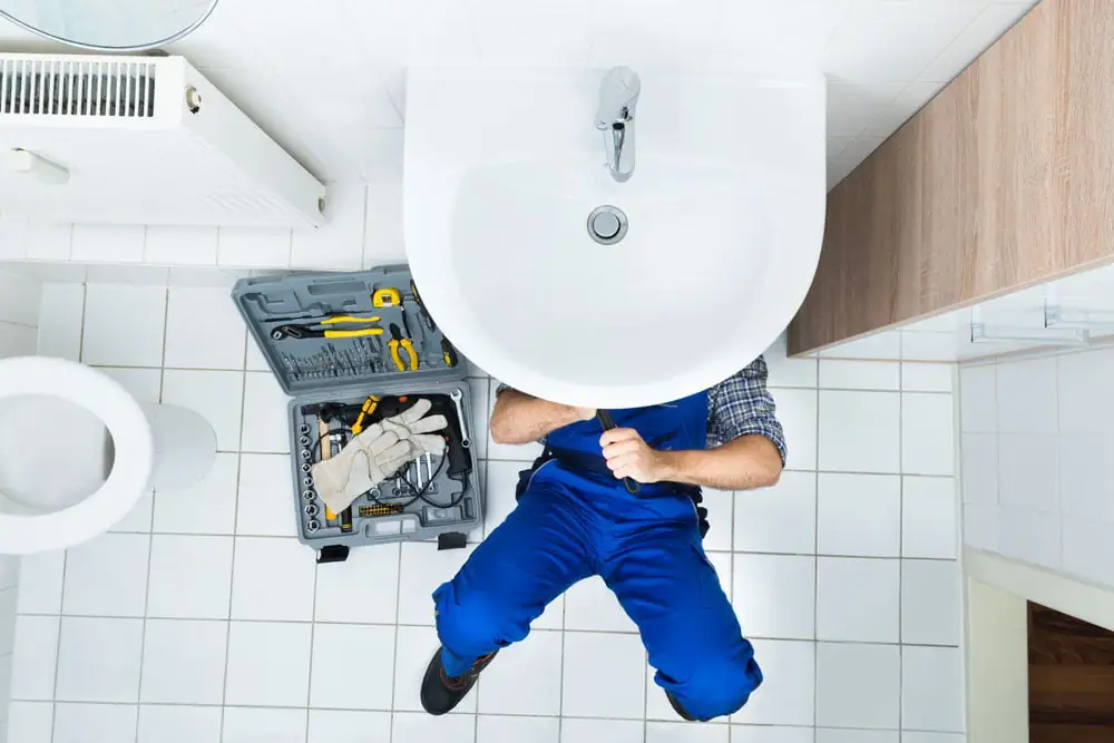 Professional plumber working under a sink in a well-equipped bathroom, showcasing expertise in bathroom maintenance and repair.